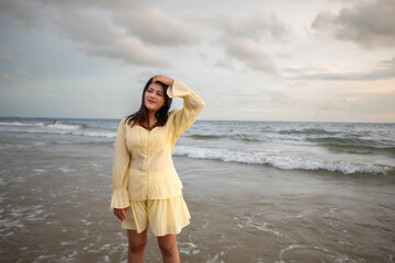 Beautiful Asian woman walking peacefully on a desert beach during sunset, with freedom concept, with amazing orange sky and sunlight reflecting on the sea and sand.