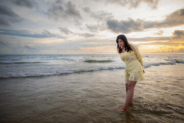 Beautiful Asian woman walking peacefully on a desert beach during sunset, with freedom concept, with amazing orange sky and sunlight reflecting on the sea and sand.