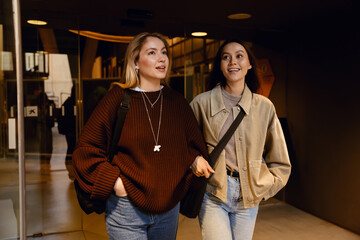 Two female friends walking and smiling while looking ahead, indoors