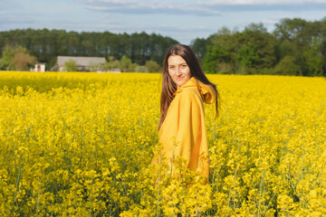 Young beautiful woman in a yellow hoodie close up in the middle of the yellow field with rapeseed...