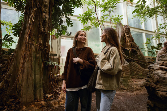 Two female friends smiling and talking, in a botanical garden