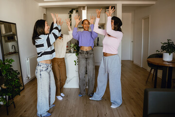 Group of four female friends standing with their hands raised and laughing