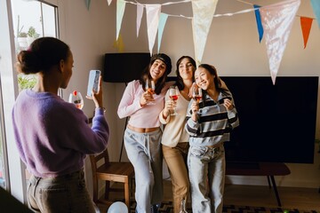A group of three female friends are smiling and posing in front of a female friend who is standing...