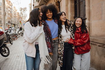 Group of four female friends walking and laughing while putting their hands on each other, on the street