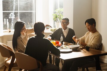 Grandfather, grandmother, their son, and grandson sitting at a table and talking while smiling