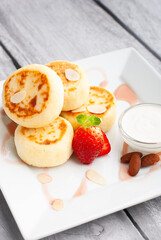 Delicious sweet cottage cheese pancakes served with fresh strawberries and cream on a white plate for breakfast