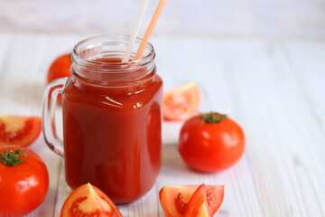 Delicious tomato juice in a glass and fresh tomatoes on a light gray table. Tomato juice on a light background. Fresh juice in a glass with a handle. Glass with juice and a straw. Vegetable drink