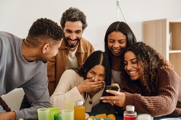 A group of five friends laughing and looking at a phone that one of them is holding