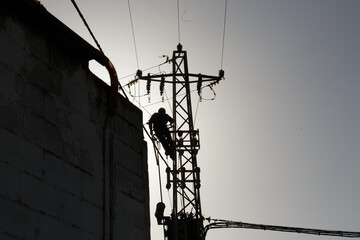 Al atardecer, figura de un Técnico de compañía eléctrica subido en un poste dañado para cambiar transformador de alta tensión, reparación de cableado eléctrico, Apagón 