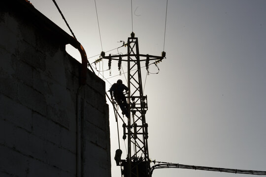 Al atardecer, figura de un T&eacute;cnico de compa&ntilde;&iacute;a el&eacute;ctrica subido en un poste da&ntilde;ado para cambiar transformador de alta tensi&oacute;n, reparaci&oacute;n de cableado el&eacute;ctrico, Apag&oacute;n 
