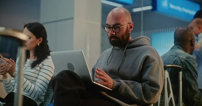 Crowded International Airport Terminal: Man Doing Remote Work on Laptop, Having Online Video Call, Waiting for Plane Flight. Diverse Passengers in Boarding Lounge of Airline Hub Using Digital Gadgets.