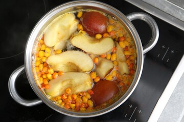 Making compot of apples and sea buckthorn berries. Simmering fruits in pot on stove, top view