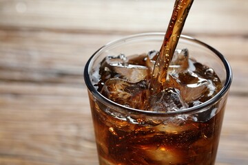 Pouring refreshing cola into glass on blurred background, closeup. Space for text
