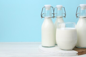 Fresh milk on white wooden table against light blue background. Space for text