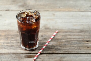 Refreshing cola with ice cubes in glass and straw on wooden table. Space for text