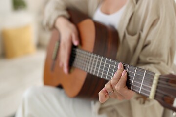 Fototapeta premium Young woman playing guitar at home, closeup