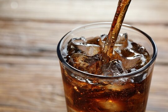 Pouring refreshing cola into glass on blurred background, closeup. Space for text