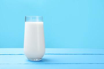 Fresh milk in glass on light blue wooden table. Space for text