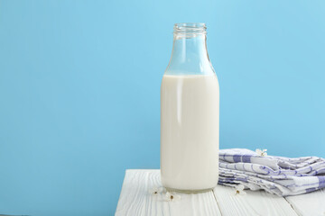 Fresh milk in bottle and blossoms on white wooden table against light blue background, closeup