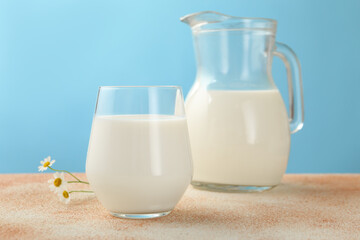 Fresh milk and flowers on table against light blue background, closeup