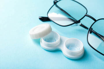 Contact lenses in case and glasses on light blue background, closeup