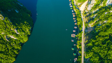 Aerial view of Lake Perućac in Tara National Park, Serbia. Stunning emerald waters, houseboats lined along the shoreline, and lush forested hills create a peaceful and scenic mountain escape