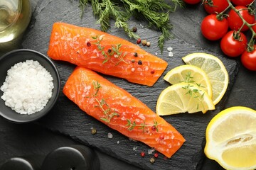 Seafood. Pieces of salmon fillet, tomatoes, lemon slices and spices on black textured table, flat lay