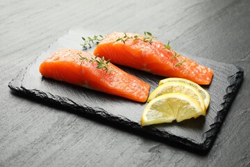 Seafood. Pieces of salmon fillet, thyme and lemon slices on black textured table, closeup