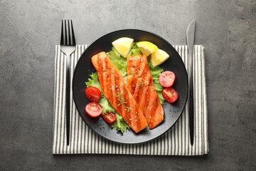 Tasty grilled salmon served with cutlery, lettuce, tomatoes and lemon on grey table, top view