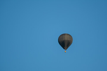 A black hot air balloon is floating in the sky above a clear blue sky