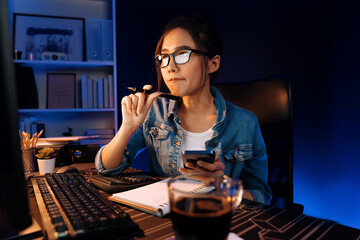 Creating young beautiful Asian creative woman thinking of sales target report on business market graph folder paperwork report, looking out of indoor with holding pen at neon at night time. Stratagem.