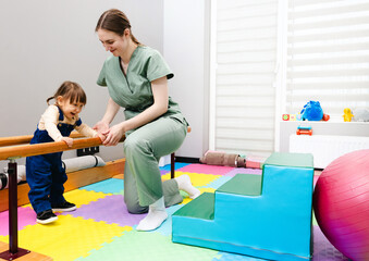 Young cute girl with cerebral palsy practices standing and balancing using handrails with...