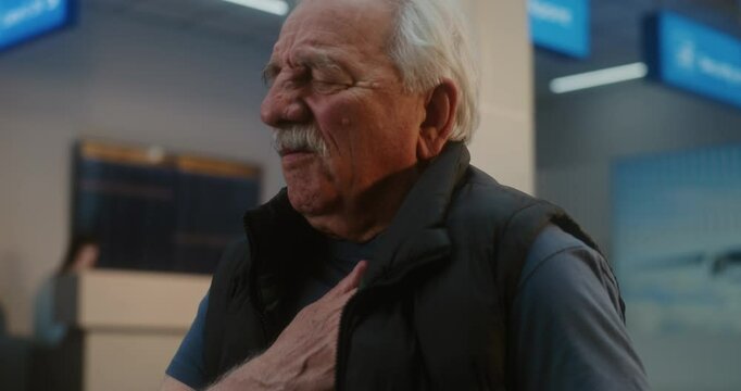 Crowded International Airport Terminal: Elderly Man Clutching His Chest, Having Heart Attack or Infarction in Boarding Lounge of Airline Hub. Diverse People and Airport Staff Helping Senior Passenger.