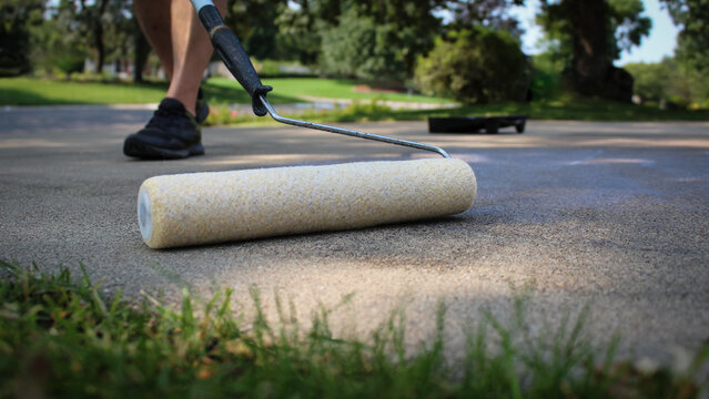 close-up of a person sealing a concrete driveway with a roller and the tray in the background. trees and everyday lifestyles scene