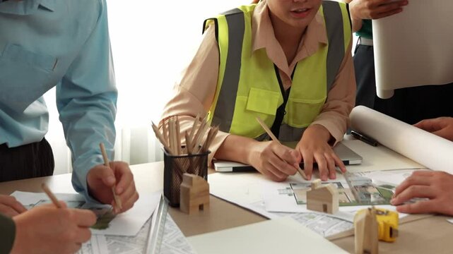Smart architect and safety engineer discussion about building blueprint on table with architectural document, measurement tools and wooden block scatter around at modern office. Closeup. Delineation.