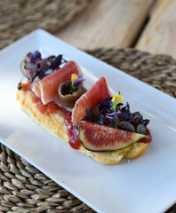 Tasty bruschetta with prosciutto and figs on white plate