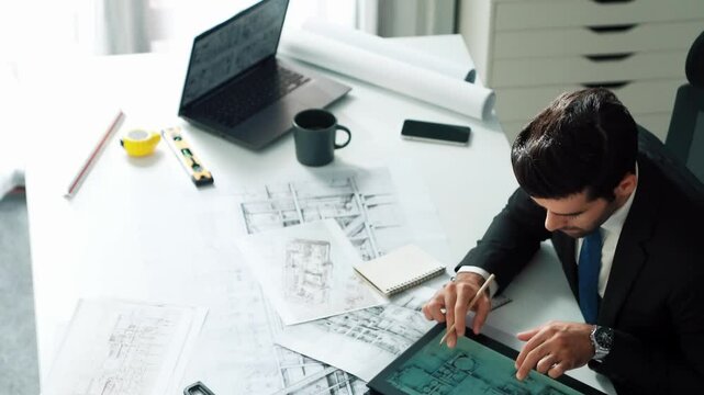 Architect engineer using laptop planning house design at office while sitting at meeting table with blueprint and equipment scatter around.Skilled civil engineer working at blueprint. Alimentation.