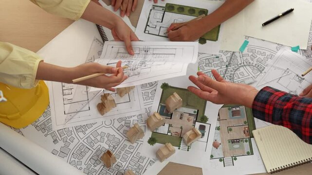 Architect and safety engineer discussion about building construction use blueprint on table with architectural document, measurement tool and wooden block scatter around at modern office. Delineation.