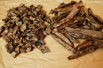 Close-up of natural dried beef lung dog treats in small chunks and long strips, displayed on brown craft paper. Healthy, single-ingredient pet snacks for dogs, ideal for training or rewarding.
