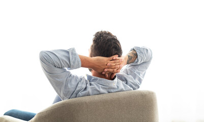 Obraz premium Weekend leisure. Happy young man sitting in armchair, relaxing and holding hands behind head, looking at window and enjoying silence. Millennial guy sitting back to camera