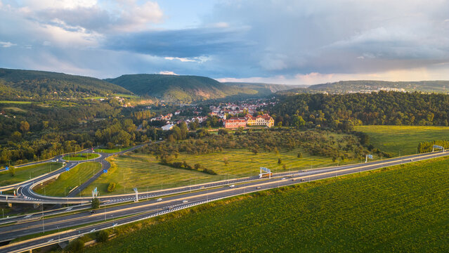A serene dusk view over Zbraslav, featuring the villages picturesque buildings with rolling hills in the background and a highway in the foreground.