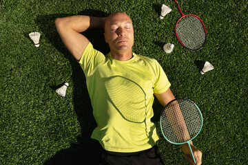 Badminton player resting after game, lying and enjoy on sport court in public park with artificial turf as green grass. Outdoors. Creative. Summer relax. View from above