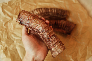 A hand holding a natural dried beef trachea - a healthy chew treat for dogs. Close-up shot highlighting the texture and quality of the single-ingredient pet snack on craft paper.