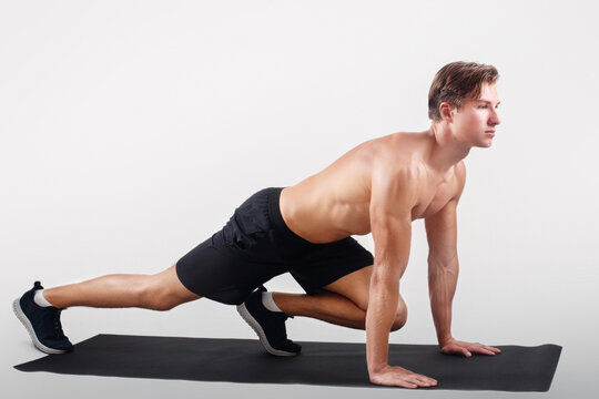 Healthy lifestyle and sports concept. Strong young man with naked chest exercising on yoga mat over light studio background. Motivated millennial sportsman doing pilates, full length