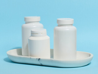 Three white plastic pill bottles of varying sizes stand on a white marble tray against a light blue background