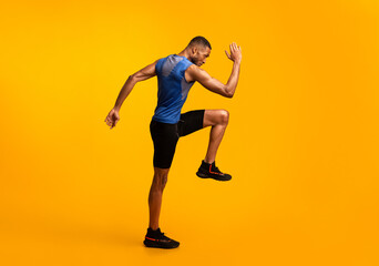 Fototapeta na wymiar High Knees. Energetic afro man doing fitness exercise, lifting leg and waving arm, free space