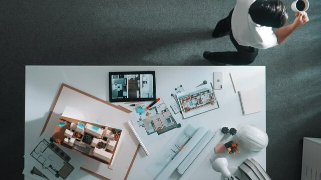 Top view of engineer drink coffee and thinking about house plan at meeting table with equipment and safety helmet scatter around. Aerial view of stressful manager walking and standing. Alimentation.