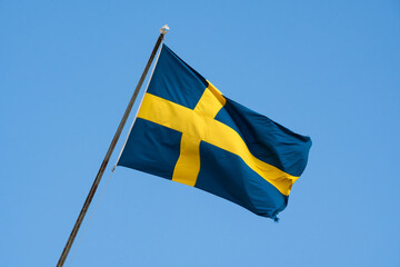 Swedish flag waving in the wind against a clear blue sky, a symbol of the Swedish nation and patriotism.