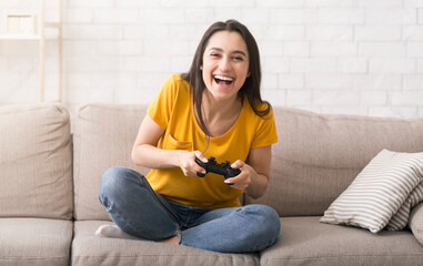 Fun stay home pastimes. Excited Hispanic woman with controller playing video games on sofa indoors