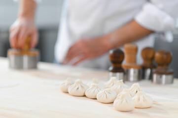 A cook rolls out dough pieces to make traditional Georgian khinkali in a kitchen. This image...